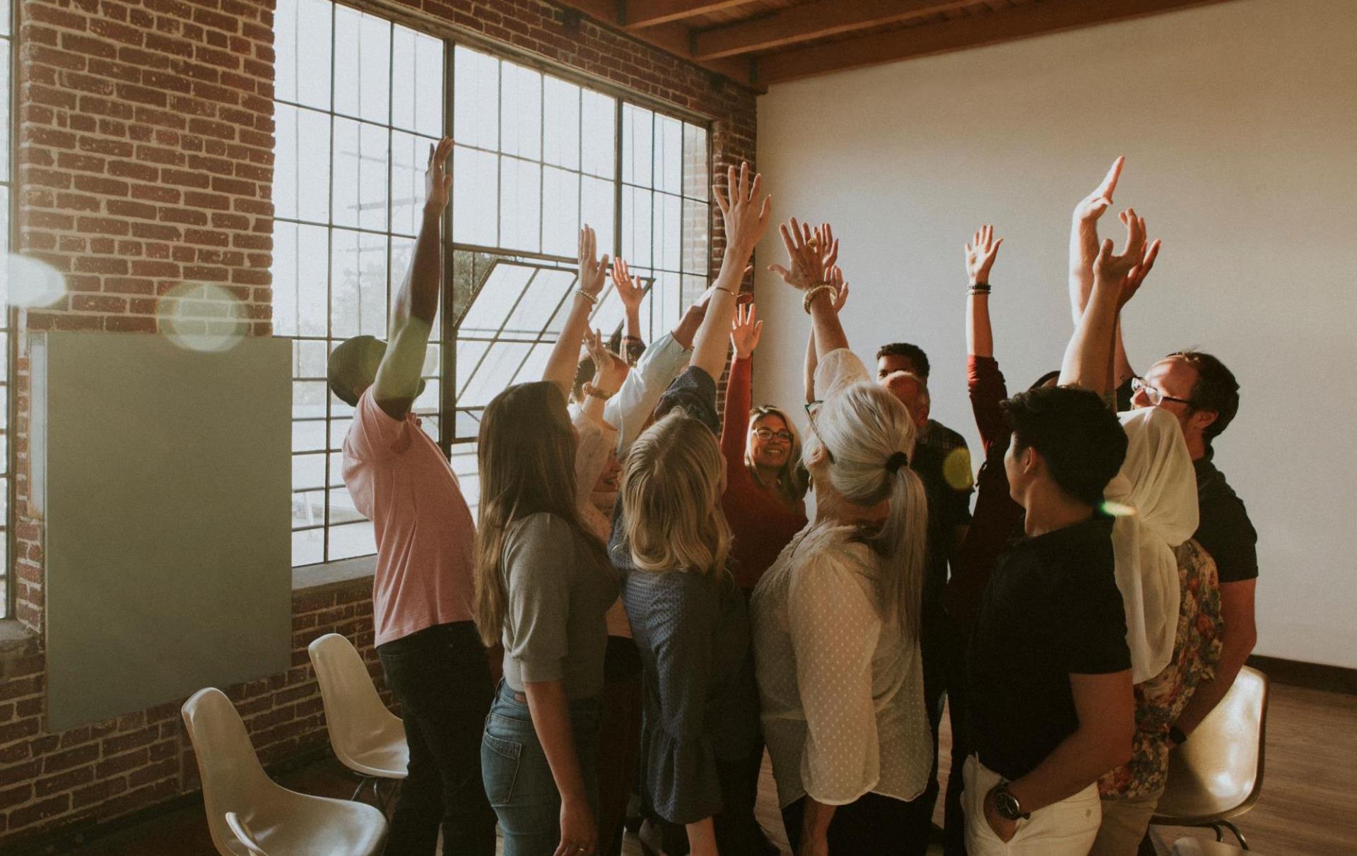 A group of happy people gathered in a circle with their hands in the air