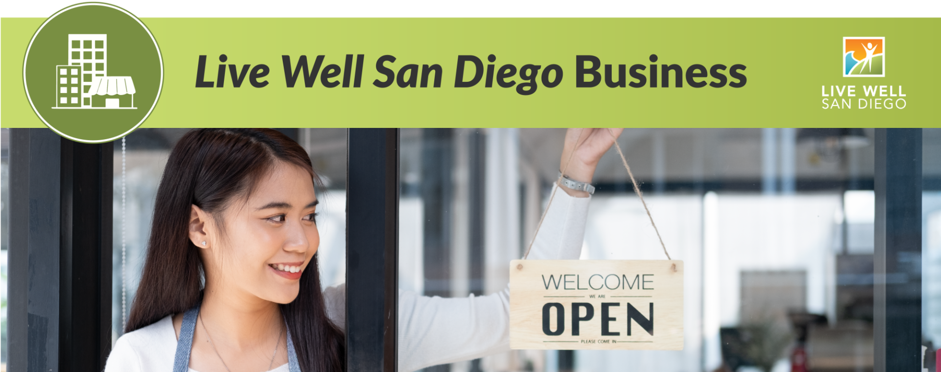 Live Well San Diego Business Banner - Woman hanging a welcome sign at her business