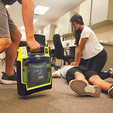 woman provides hands-only CPR as an AED is brought in