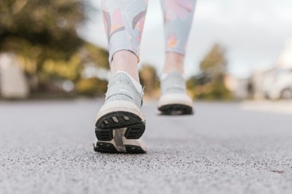 A person with pink and gray leggings and shoes walking on gray asphalt
