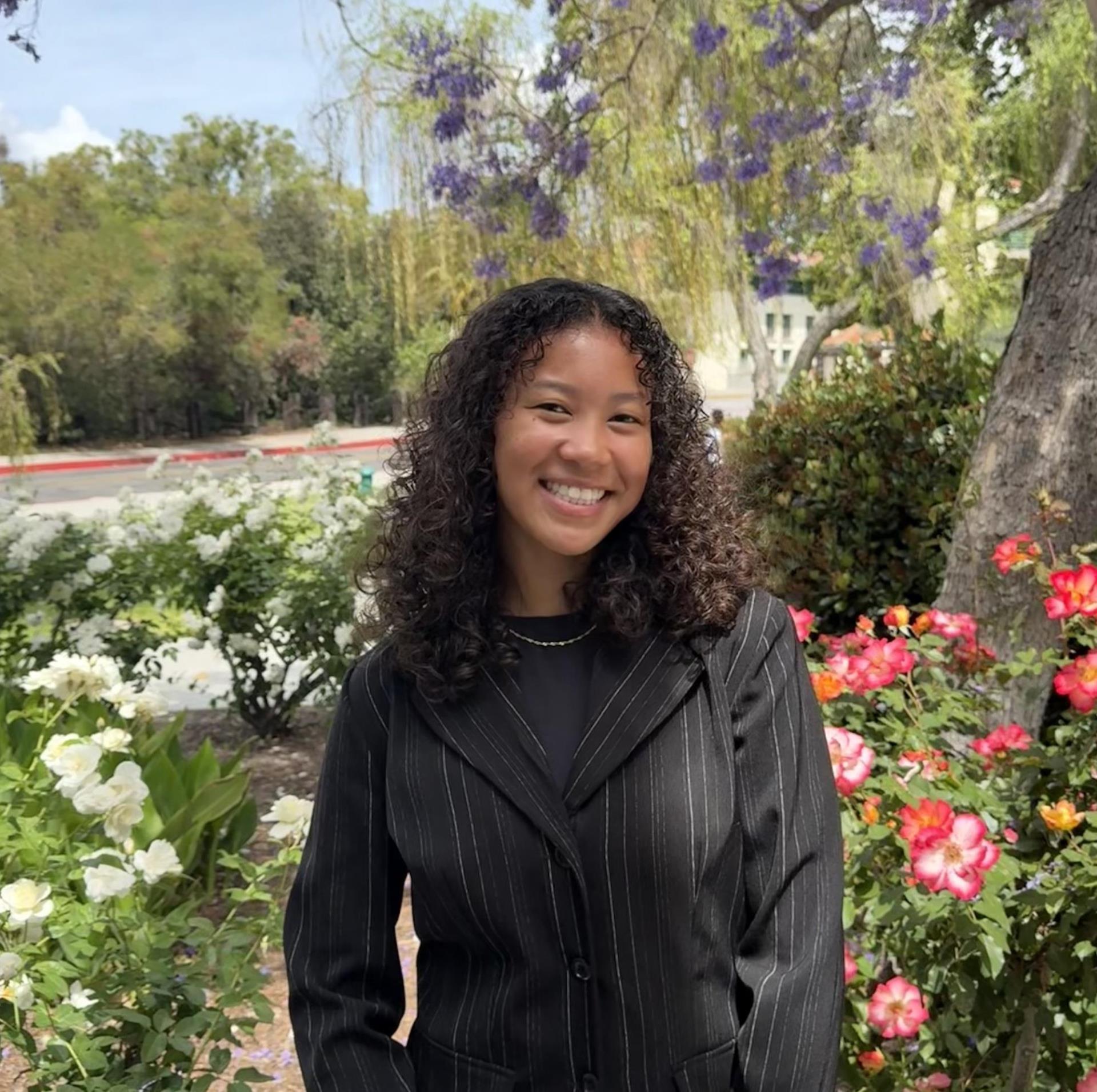 Headshot of Kitiara Cox, Youth Sector Coordinator, standing in front of trees and flowers