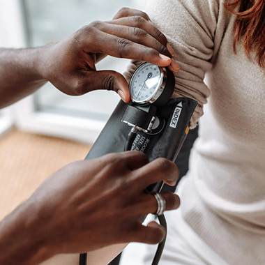 A healthcare professional checks a person’s blood pressure using a cuff and gauge, adjusting the equipment wrapped around the person’s arm.