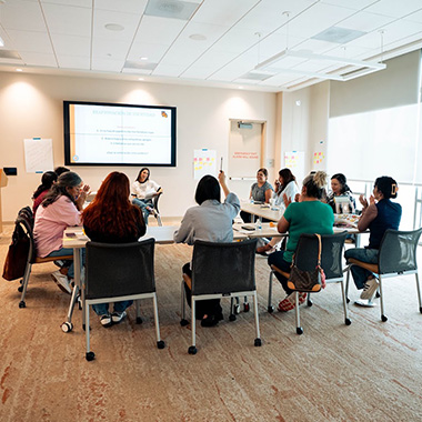 LUMI participants seated in a meeting room arranged in a circle, participating in a discussion with a presentation screen in the background.